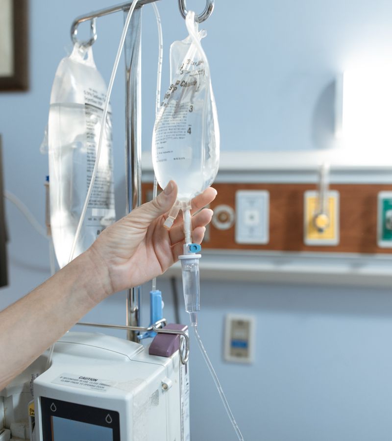 Close-up image of an IV drip and hand in a hospital room, illustrating medical care.