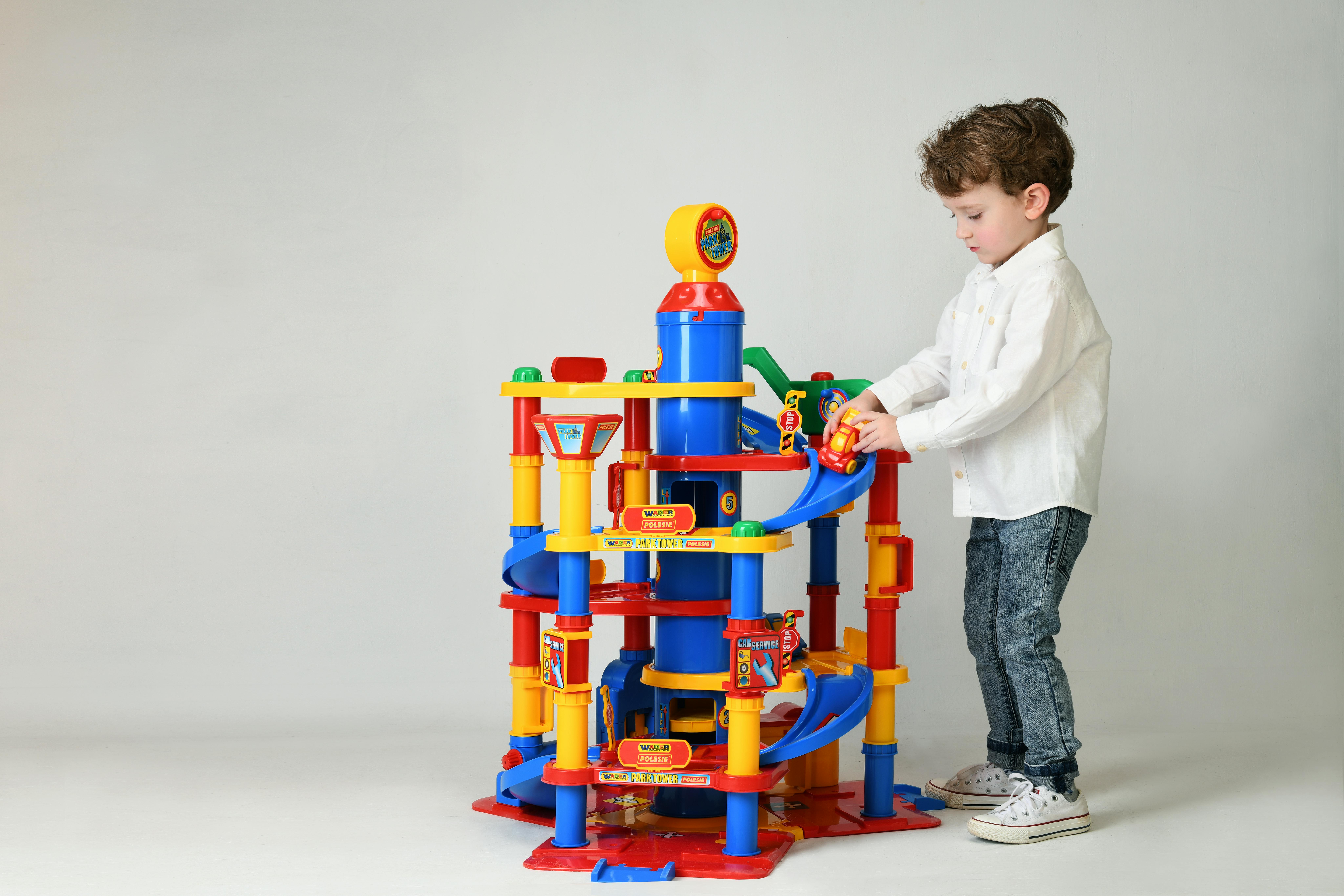 Young boy in a white shirt playing with a colorful toy car tower set in a studio.