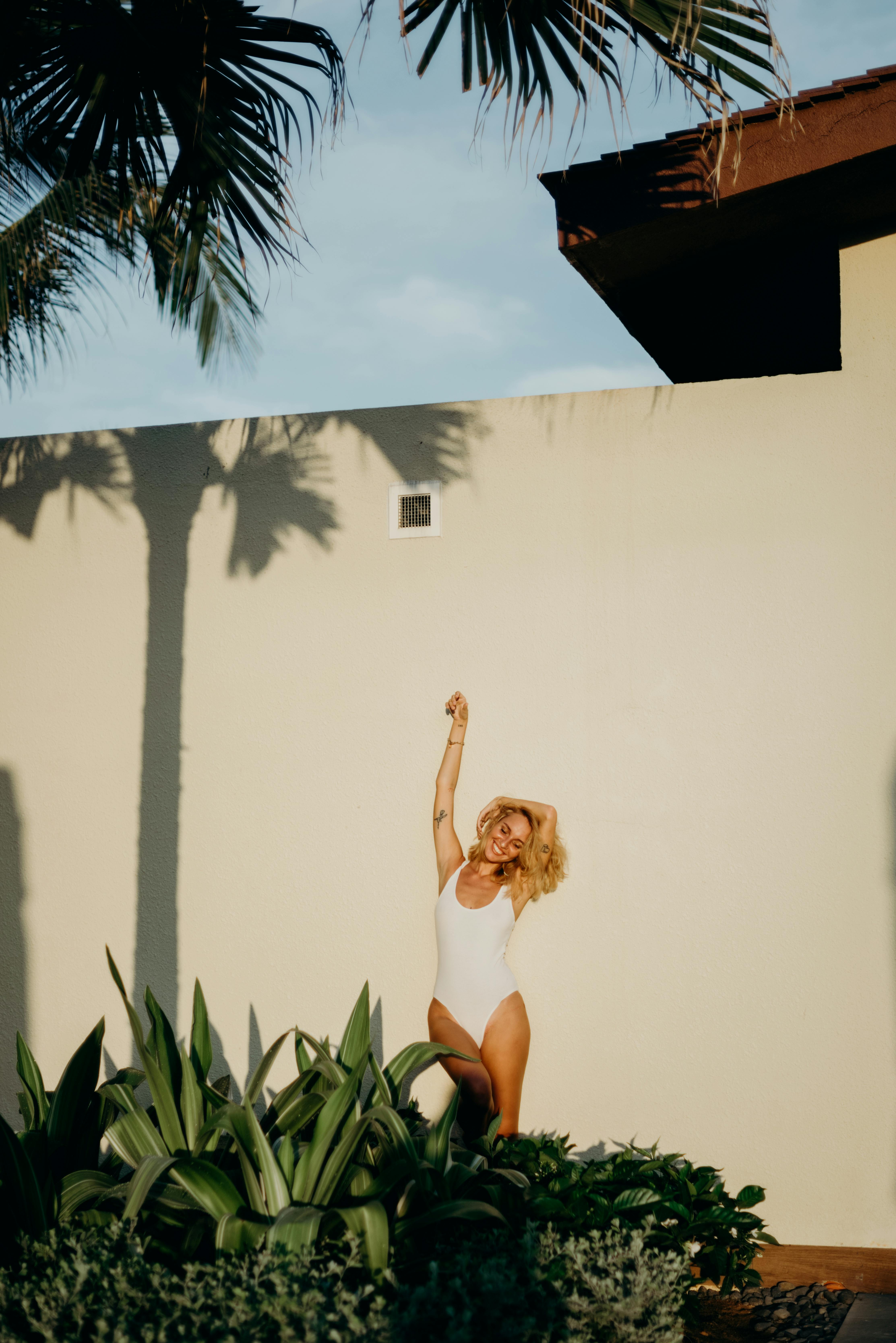 Woman in White Tank Top and Black Skirt Standing Beside White Wall