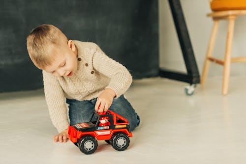 Child in Beige Sweater Playing Red Toy Car