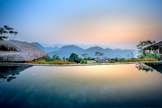 Clean water of pool located on tropical resort with wooden bungalows against silhouettes of mountain ridge on evening time in nature