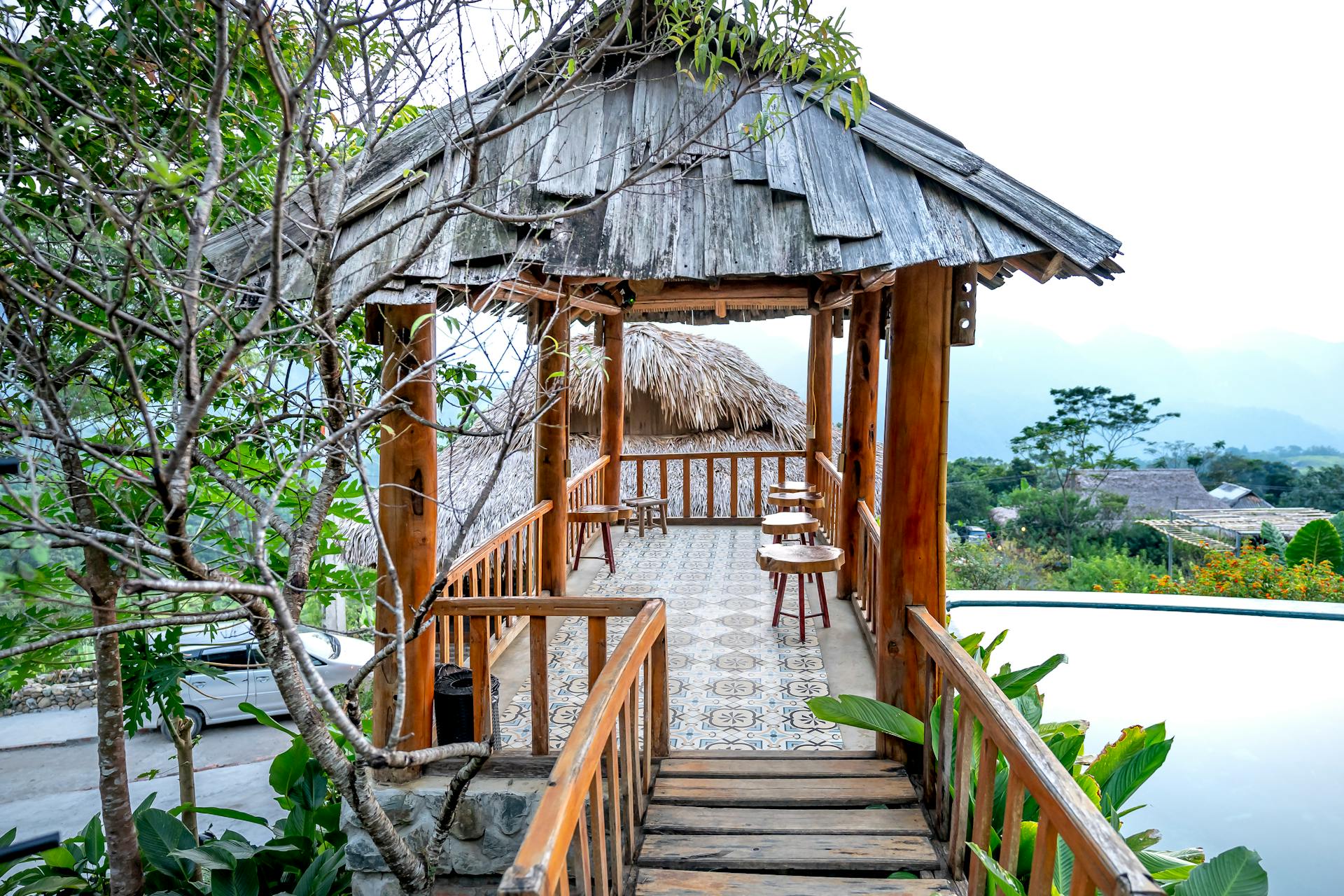 A serene tropical gazebo with wooden chairs by the poolside, surrounded by lush greenery.