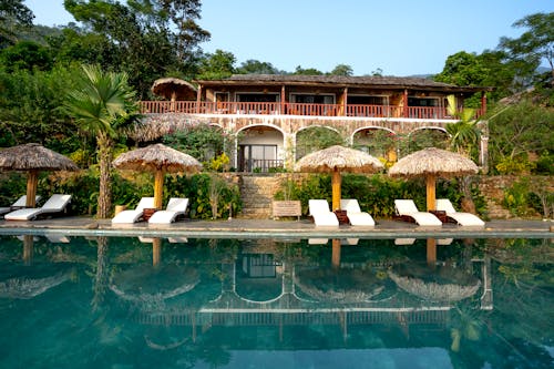 Pool and sunbeds with straw umbrellas in tropical hotel