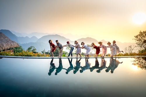 Free Group of happy people standing in chain above still water of lake and having fun in summer evening Stock Photo