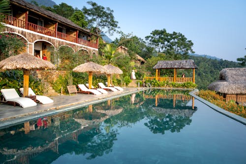 Swimming pool and sunbeds with parasols near small hotel in south eastern style in tropical resort