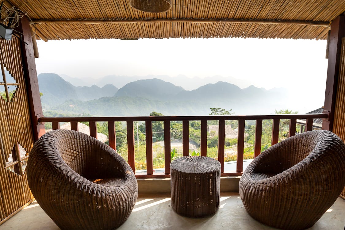 Free Comfortable armchairs and small side table on veranda near wooden barrier overlooking mountain ridge and green trees in tropical country Stock Photo