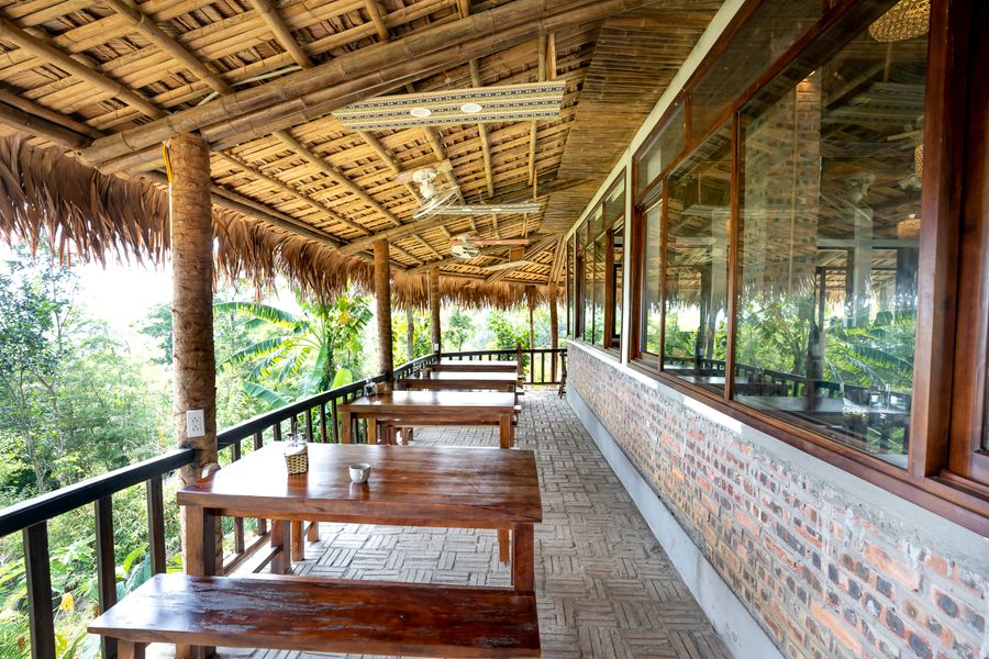Shaded terrace tables with wooden chairs beside tropical greenery