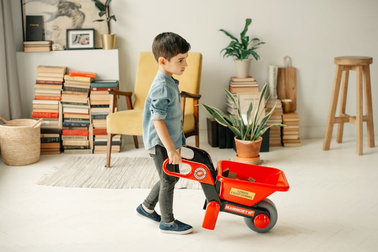 Boy In Blue Denim Shirt Playing With His Plastic Wheel Barrow