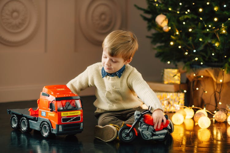 Boy In White Sweater Playing With His Vehicle Toys