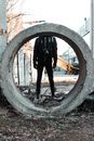 Unrecognizable male with photo camera in casual outerwear standing near reinforced concrete ring on street in industrial district in city