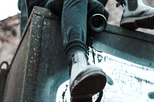 Free From below of anonymous male with professional photo camera sitting on black stone structure on street in city on blurred background Stock Photo