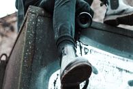 From below of anonymous male with professional photo camera sitting on black stone structure on street in city on blurred background
