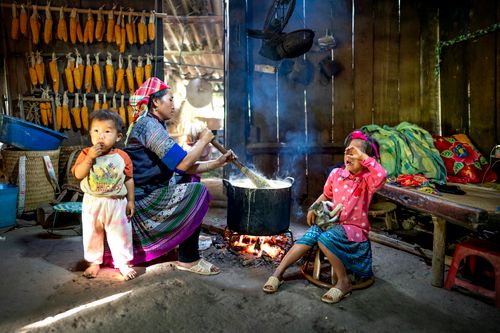 Free Side view of Asian woman in colorful outfit sitting with children and preparing food on bonfire in wooden rural barn in daytime Stock Photo