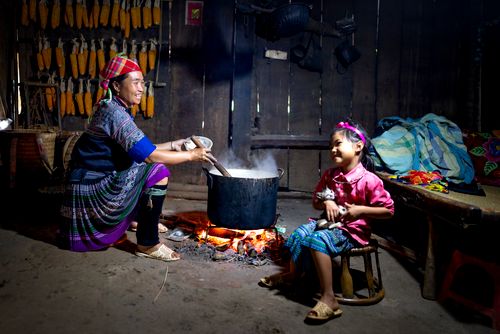 Free Side view of Asian woman in casual clothes sitting and preparing food while little girl sitting with small cat on street against wooden fence Stock Photo