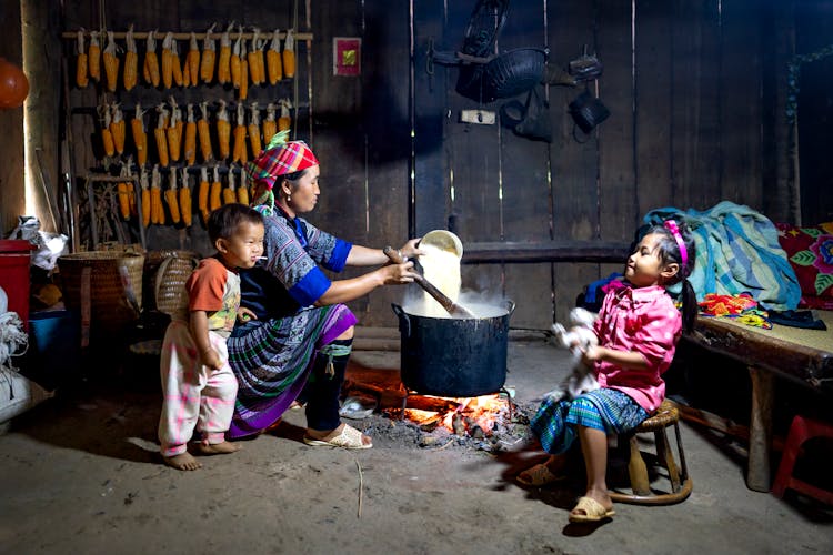 Ethnic Mom Cooking Rice Against Children In Poor House