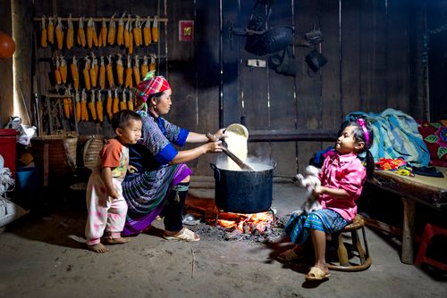 Free Ethnic mother pouring rice into pot on fire against daughter with cat and barefoot baby eating lollipop at home Stock Photo