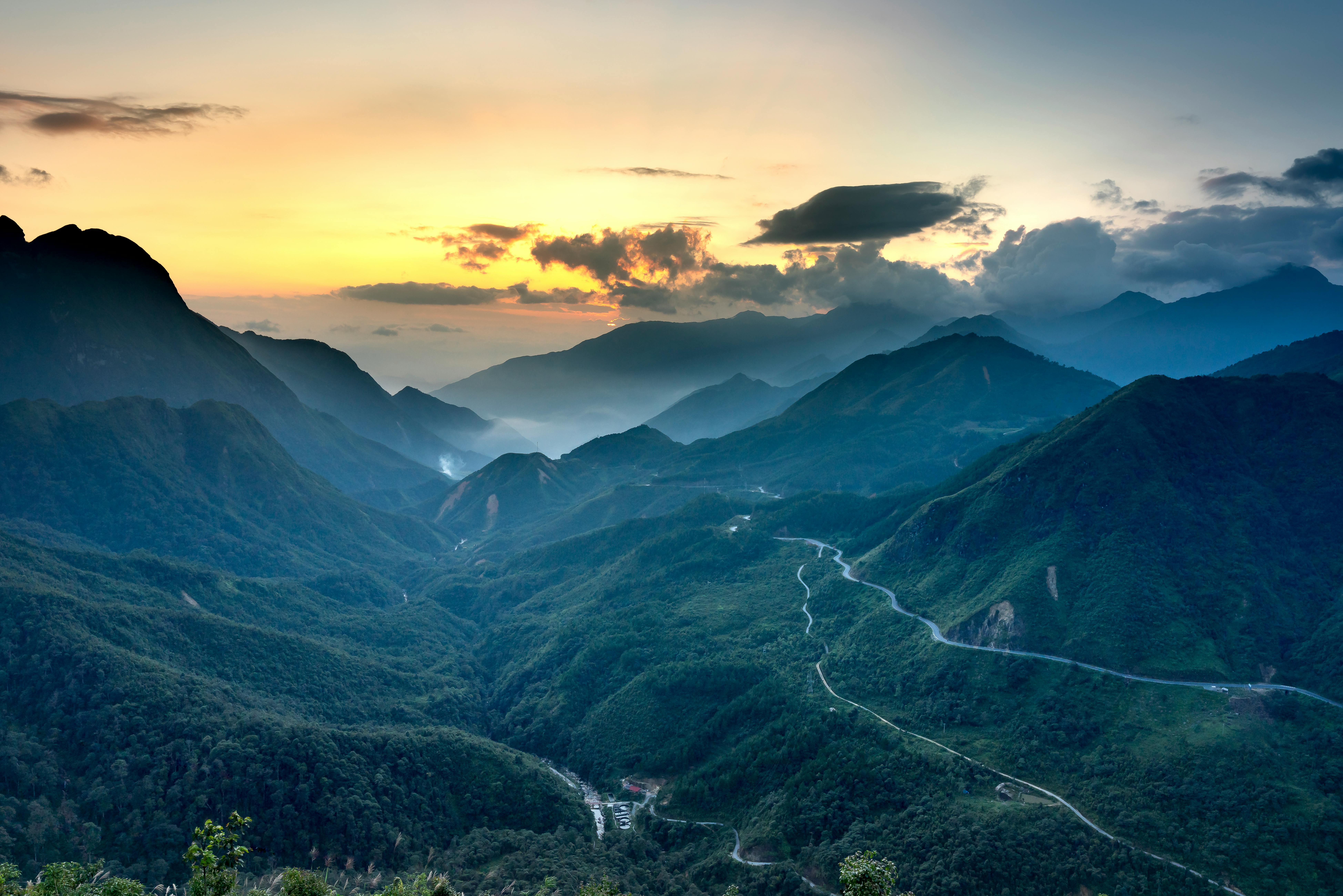 Green ridges with wavy roads under fluffy clouds at sunset · Free Stock Photo