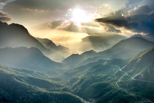 Free Breathtaking view of majestic mountains with bended roads under cloudy sky with glowing sun in evening Stock Photo