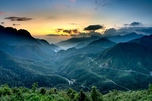 Free Spectacular view of magnificent mountains with lush green trees and wavy roadways under colorful sky with clouds at sundown Stock Photo