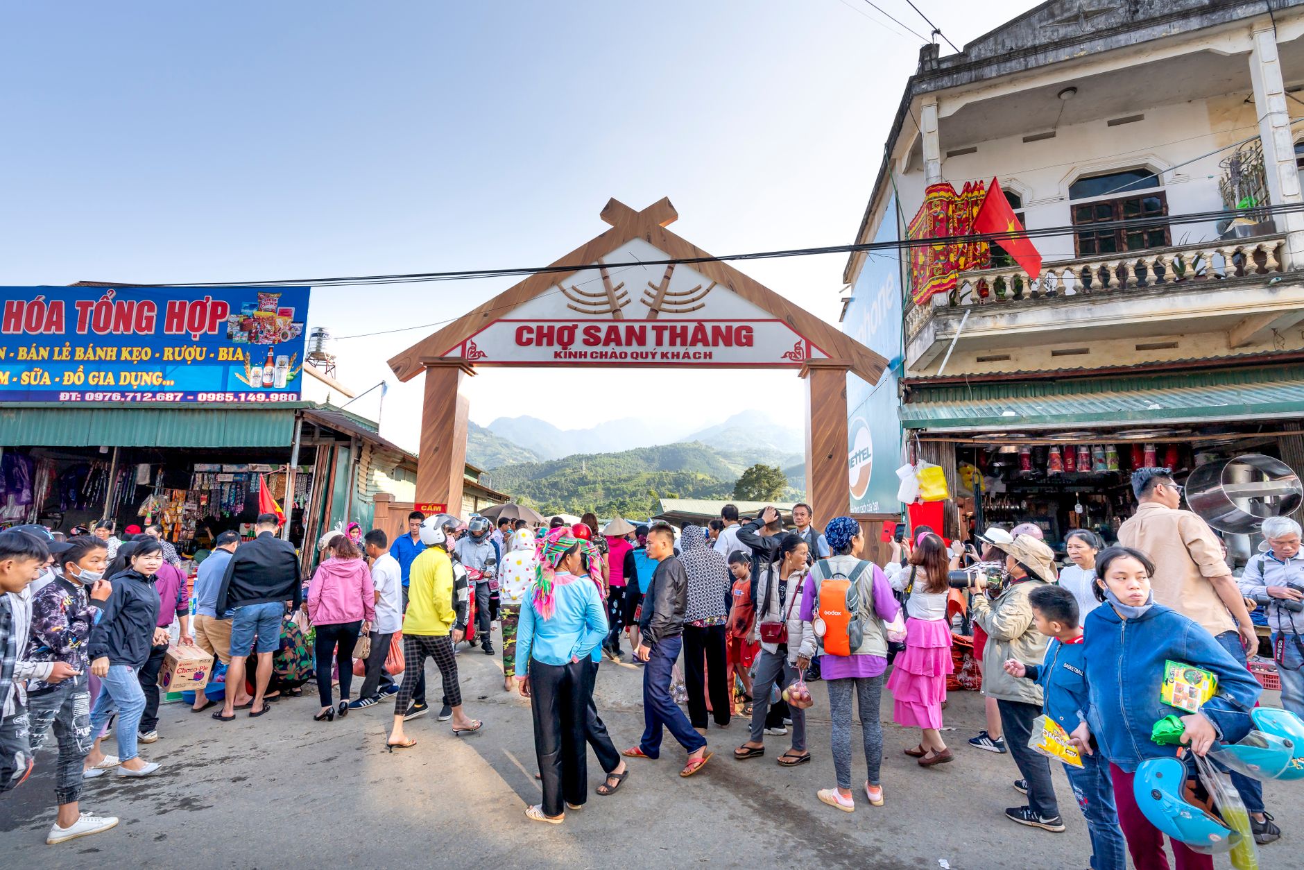 Anonymous ethnic people strolling on walkway against buildings and misty mountains in local bazaar in town
