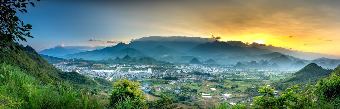 A breathtaking view of a village nestled among mountains at sunset, with lush greenery and a dramatic sky.