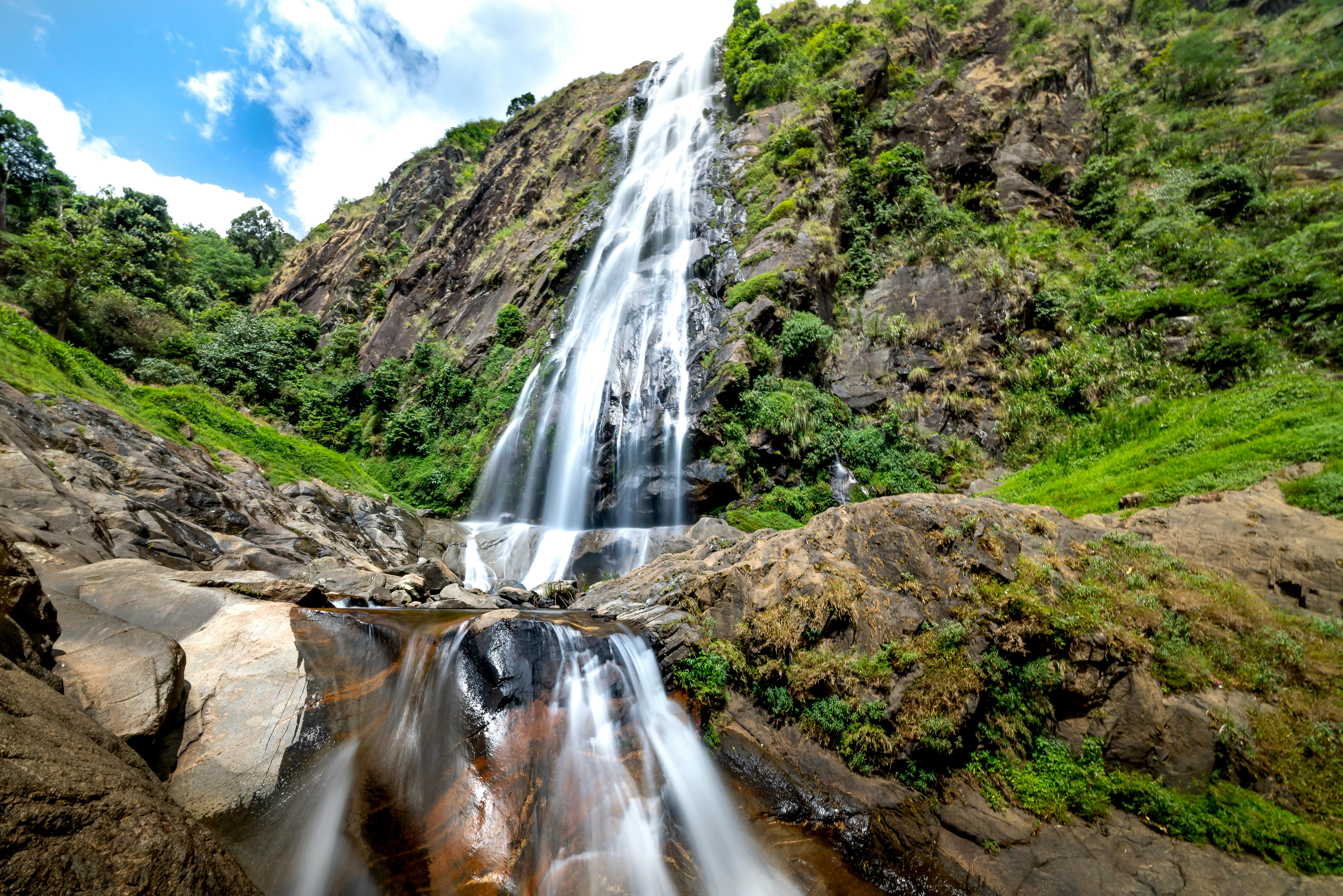 fast waterfall on mount with grass under cloudy blue sky