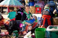 Ethnic vendor breastfeeding son against anonymous partner in market