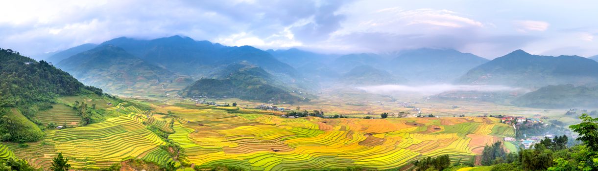 Scenery view of wavy agricultural fields against massive mountains with trees under cloudy sky in countryside in misty weather