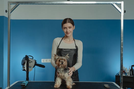 A professional groomer poses with a groomed Yorkshire Terrier in a modern grooming salon.