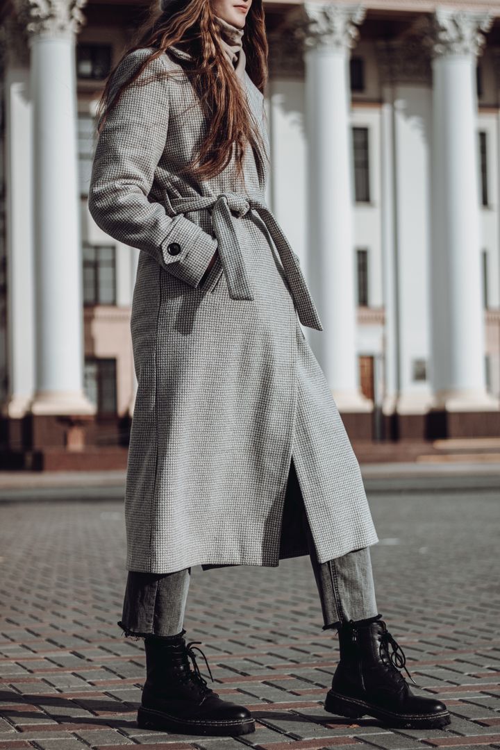 Model in a long pale coat walking past concrete — photo by Igor Kirillov on Pexels