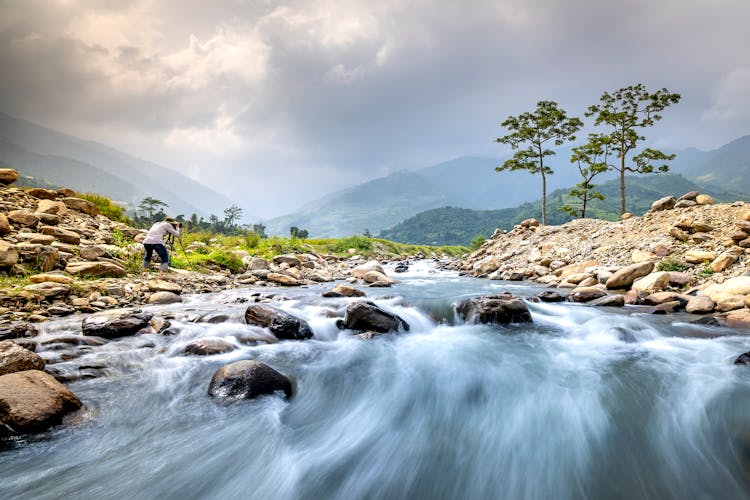 Photographer Taking Photos At Edge Of Swift Mountain Stream 