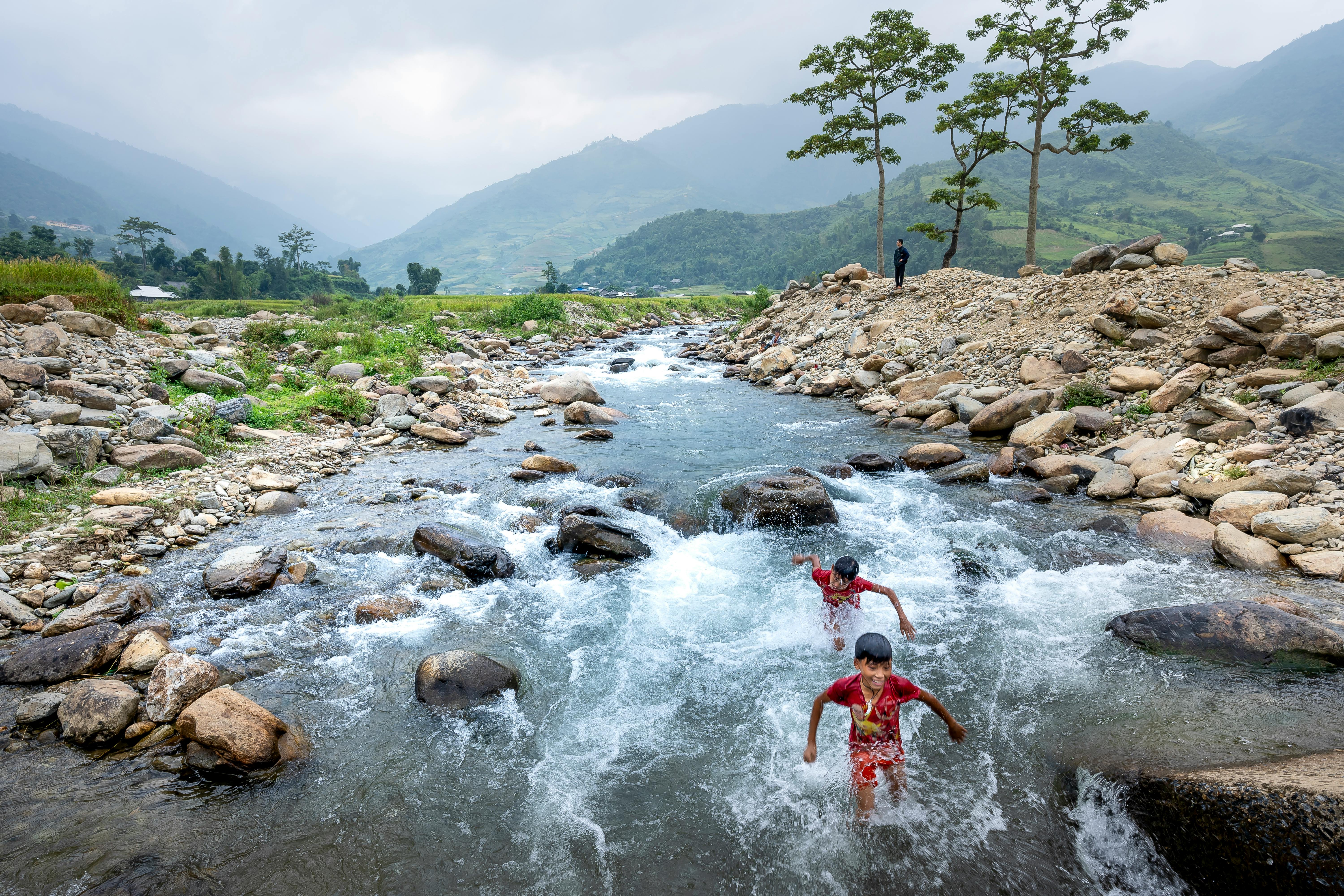 Two boys play in a scenic mountain stream surrounded by rocks and greenery.