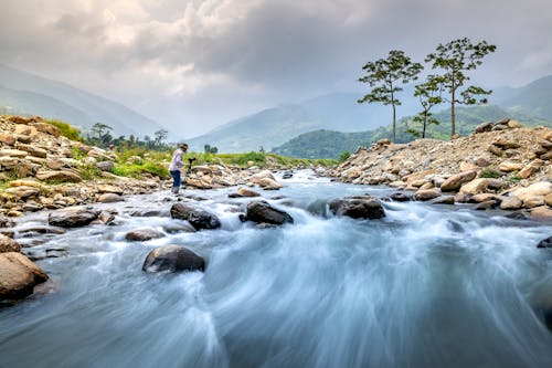 Free A Man With a Tripod and Camera Standing Along a Flowing River Stock Photo