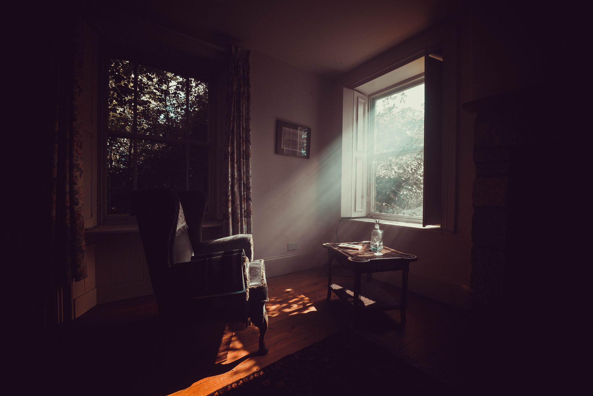 A serene vintage room with sunlight streaming through the window, highlighting a cozy armchair and wooden furniture.