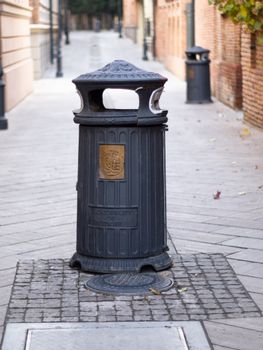A classic urban street trash can with decorative design in a deserted alley.