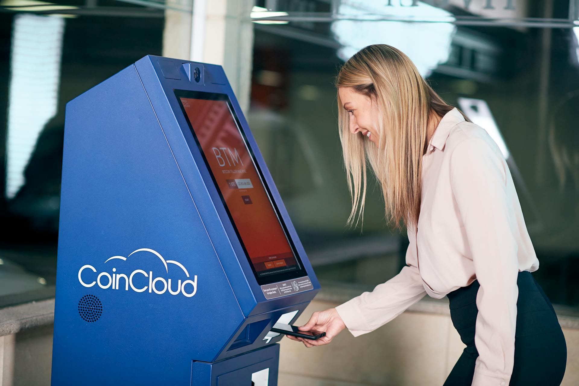 Woman smiling while using a CoinCloud cryptocurrency ATM indoors.