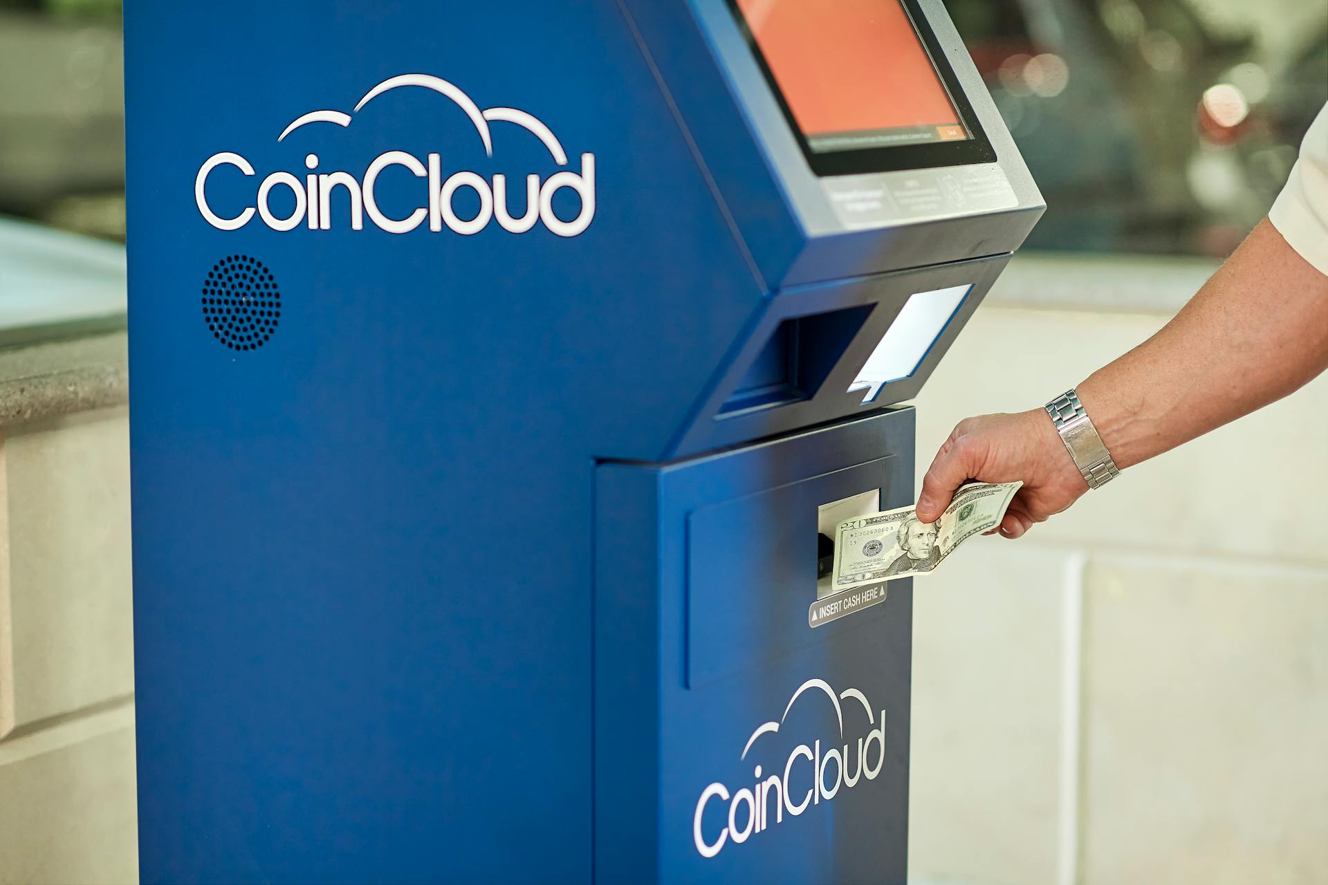 A person using a CoinCloud Bitcoin ATM to insert cash for cryptocurrency transactions.