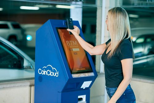 Free Blonde woman transacts at a CoinCloud cryptocurrency ATM, indoors in a parking area. Stock Photo