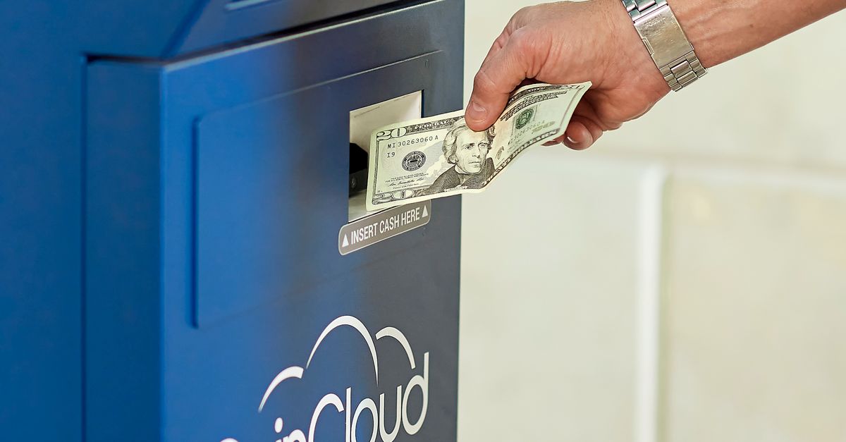 Hand inserting cash into a CoinCloud ATM, illustrating cryptocurrency exchange process.