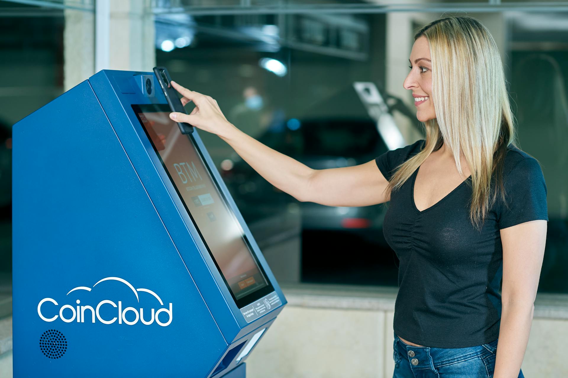 Blonde woman interacting with a digital currency ATM for modern financial transactions.