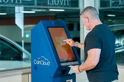 Free Man interacts with a CoinCloud Bitcoin ATM indoors, facilitating cryptocurrency exchange. Stock Photo