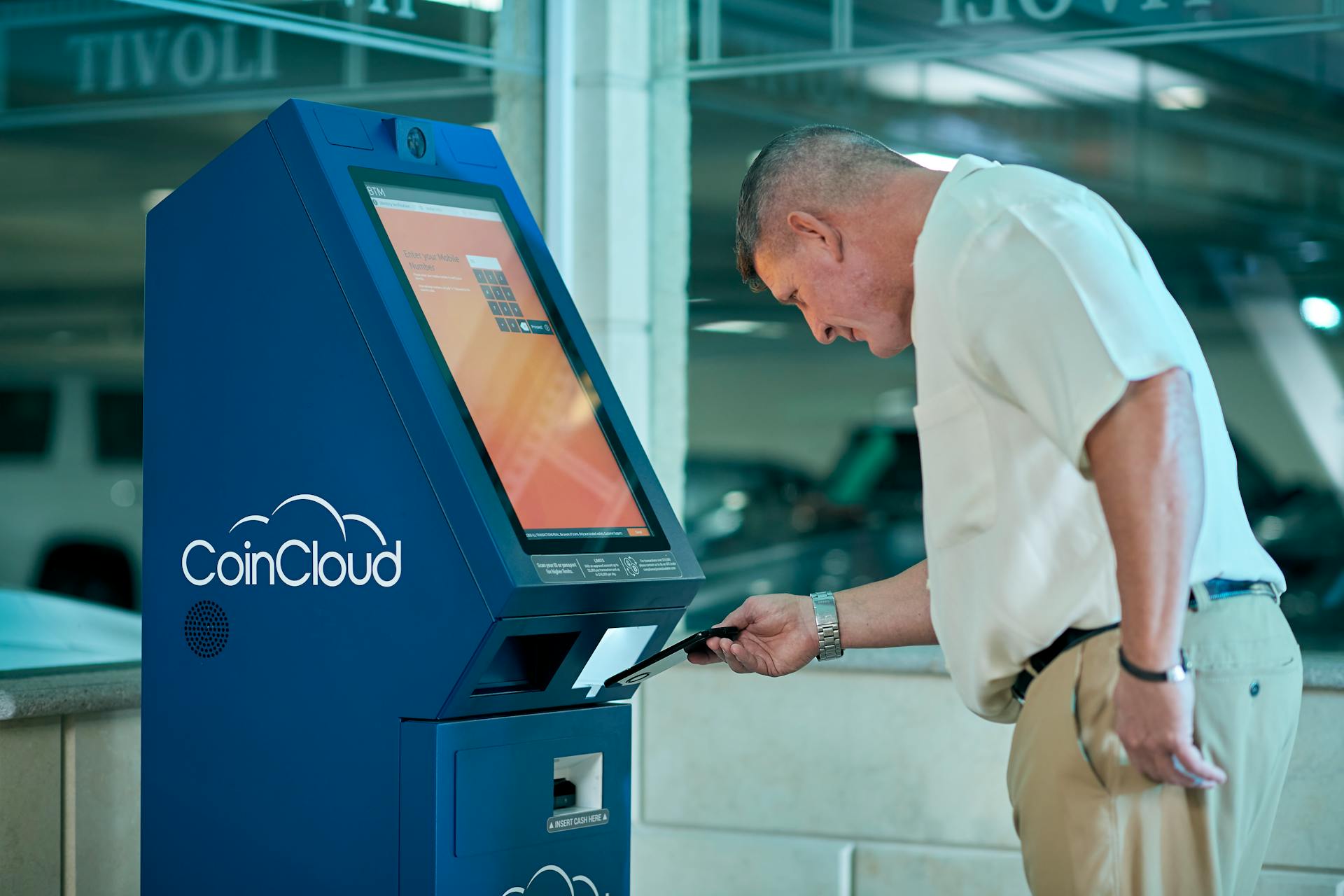 Adult man interacting with Coin Cloud digital currency machine indoors, demonstrating modern technology usage.