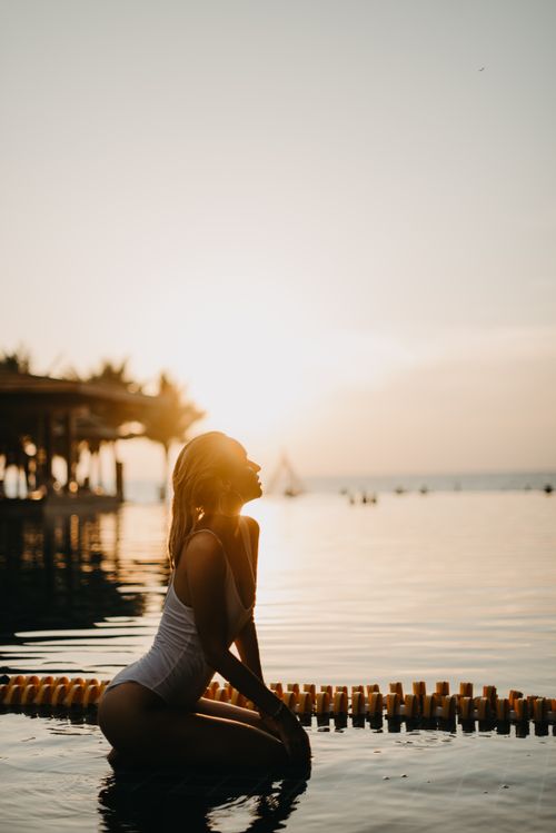 Free A woman in swimwear sits by the water at sunset on a Bali beach, creating a peaceful scene. Stock Photo
