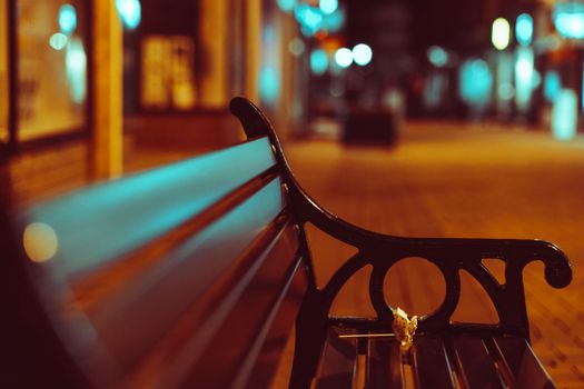 Close-up of a city bench at night with beautiful bokeh lights creating a moody urban scene.