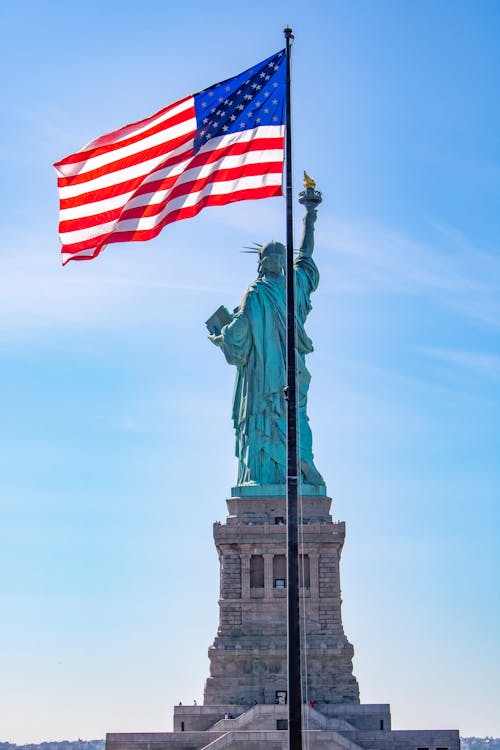 Free The Statue of Liberty Behind an American Flag on a Pole Stock Photo