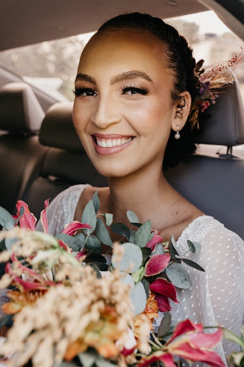 Free Young feminine woman with makeup and blossoming flowers looking at camera with toothy smile in transport on wedding day Stock Photo