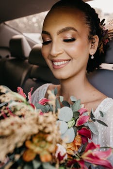 Crop young smiling bride with long eyelashes and closed eyes sitting in vehicle with blossoming flowers during festive occasion