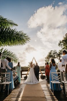 Back view of anonymous bride with groom and elegant black guests during festive event on veranda under blue cloudy sky