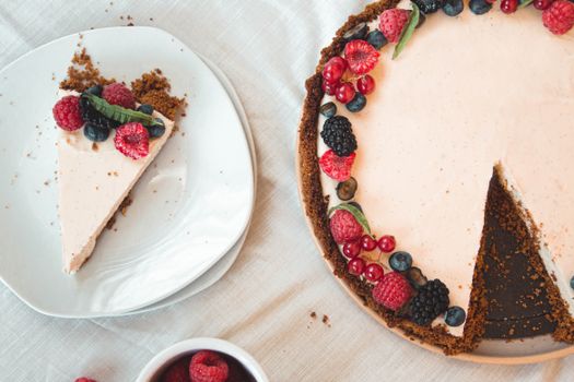 Top view of a berry-decorated cheesecake with a slice on a white plate.