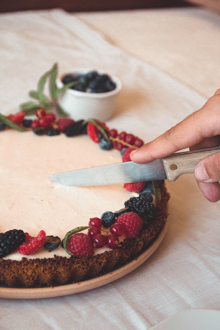 A Person Cutting A Tart With Berries